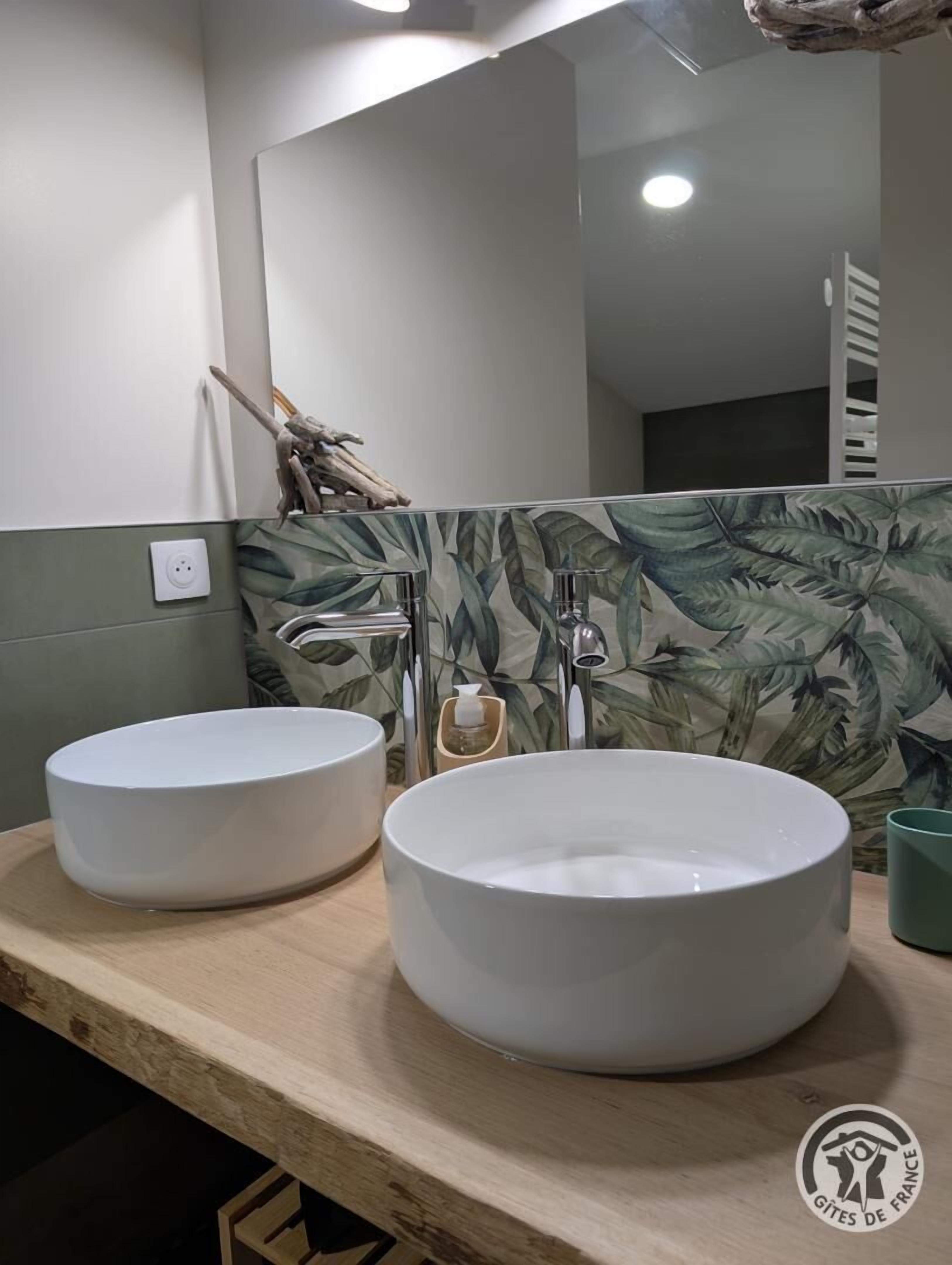 Een badkamer met twee witte wasbakken, een spiegel en een groene betegelde muur met een bladmotief.