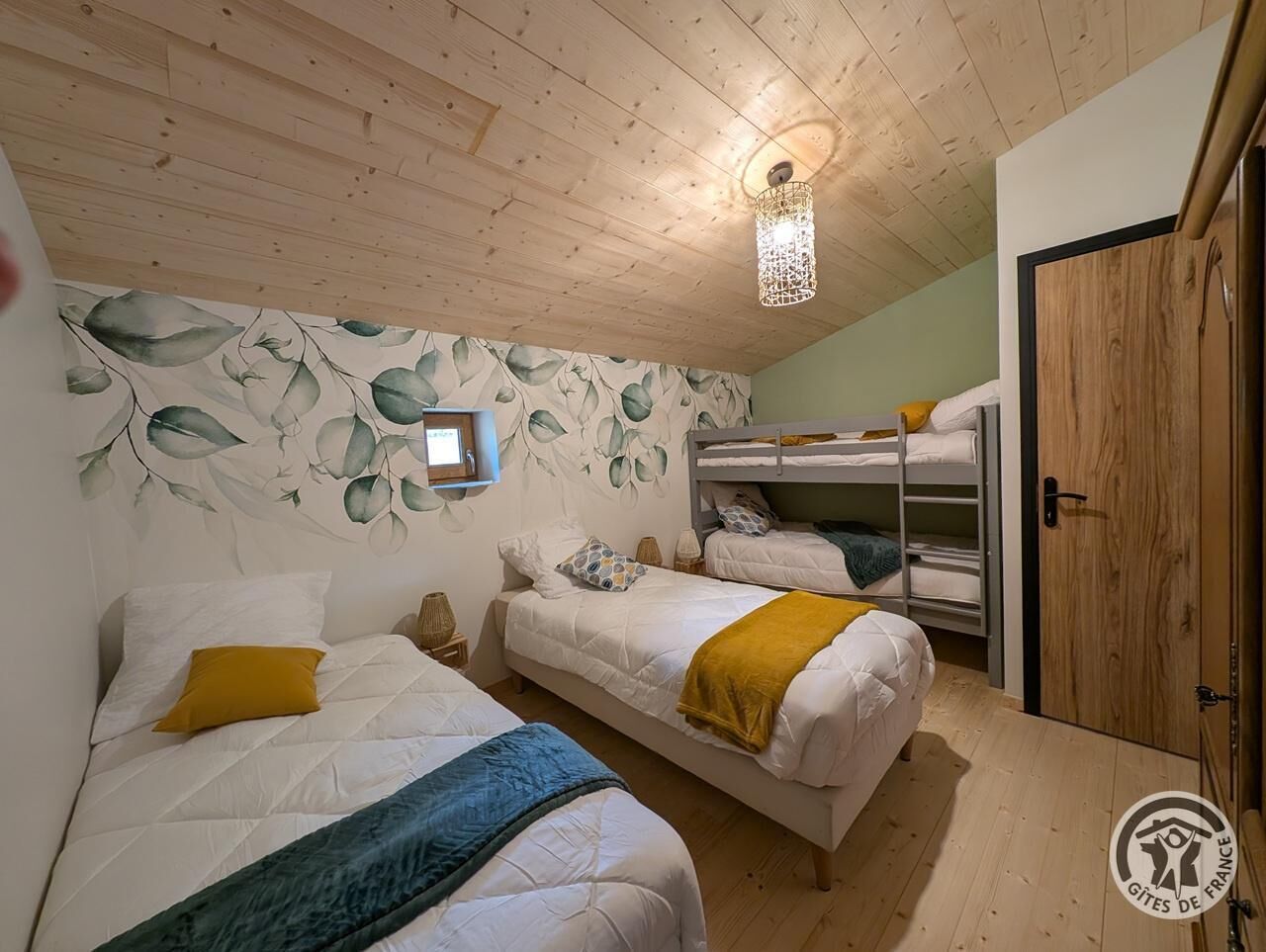 Een kamer met twee bedden, een stapelbed, houten plafond en een wand met bladmotief.