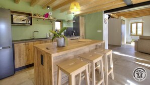 A modern kitchen with wooden beams, a central island with stools, a microwave, and a hanging light fixture. - "Ensemble - MEYS - Gîte (MEYS)