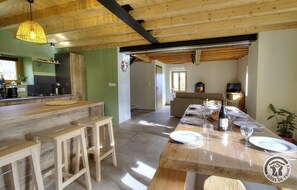 A rustic kitchen with wooden beams, a bar area with stools, and a dining table set for six with wine glasses and plates.