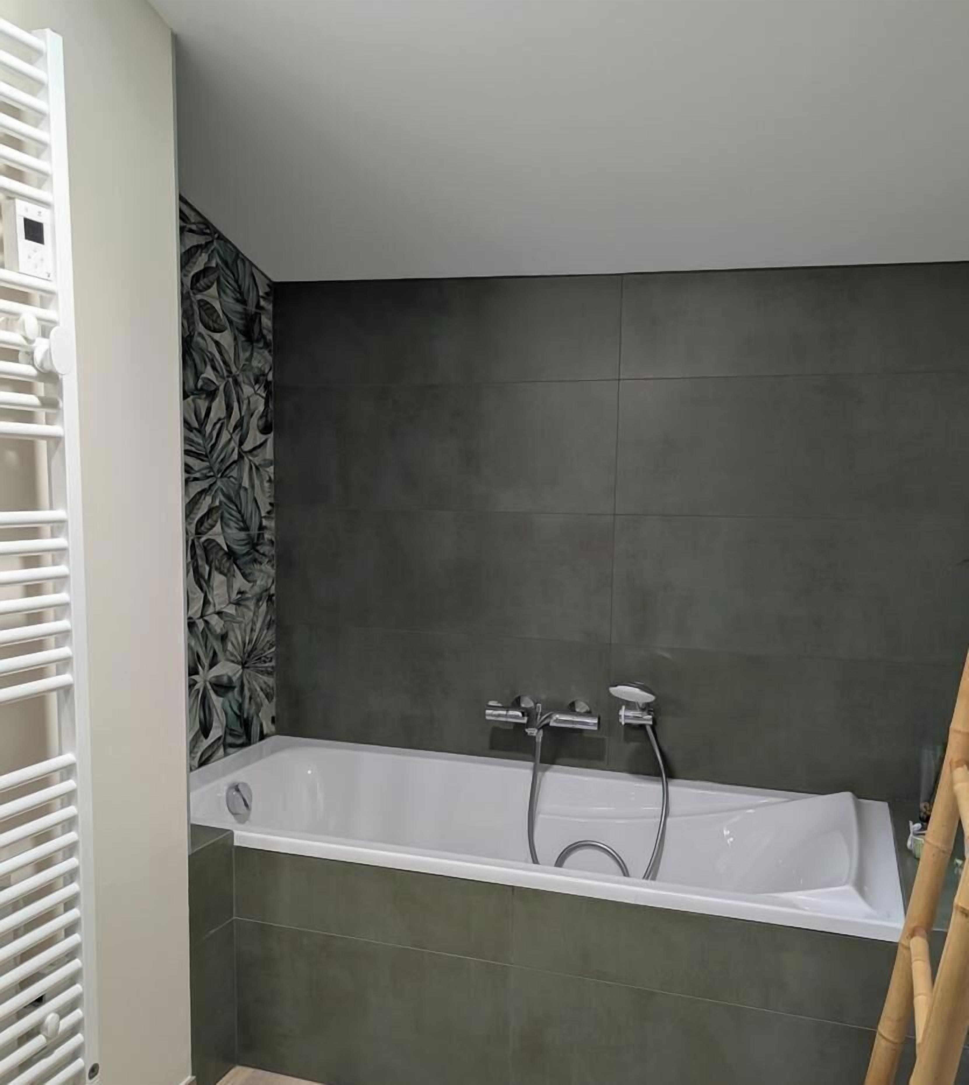 A modern bathroom with a freestanding bathtub, dark tiled walls, and a white towel rack.
