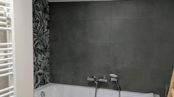 A modern bathroom with a freestanding bathtub, dark tiled walls, and a white towel rack.