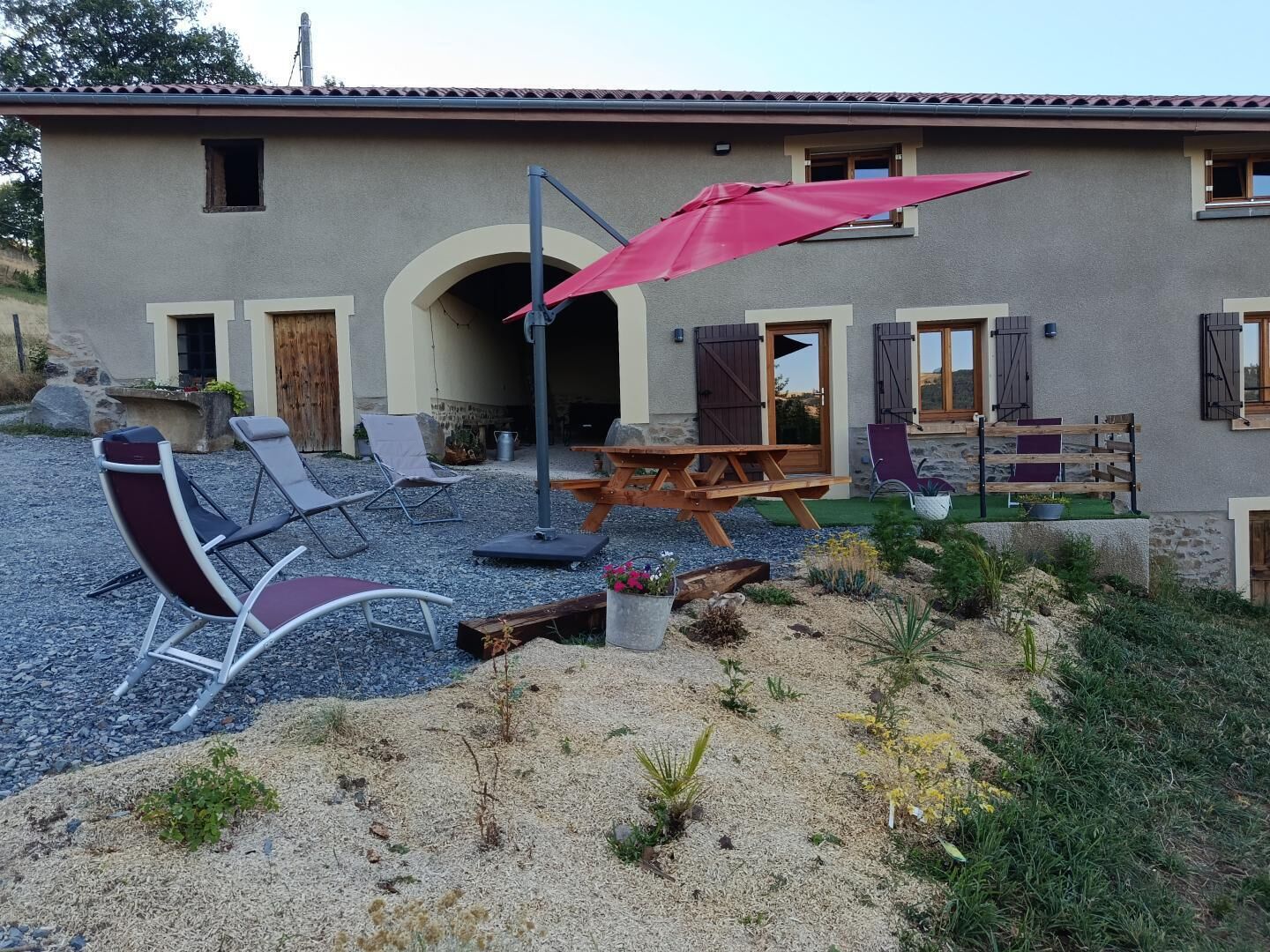 A building with a patio area featuring outdoor furniture and a red umbrella.