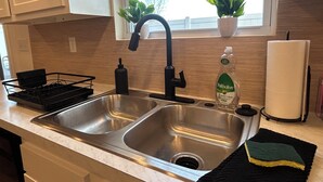 A kitchen with a double sink, a dish rack, a bottle of Palmolive dish soap, and a towel.