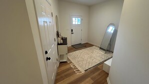A hallway with wooden flooring, a white door, a small rug, and a mirror leaning against the wall.