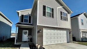 A two-story residential house with a garage, a front porch, and a brick foundation.