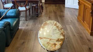 A dining area with a wooden table and chairs, a marble accent piece, a leather sofa, and a wooden cabinet.