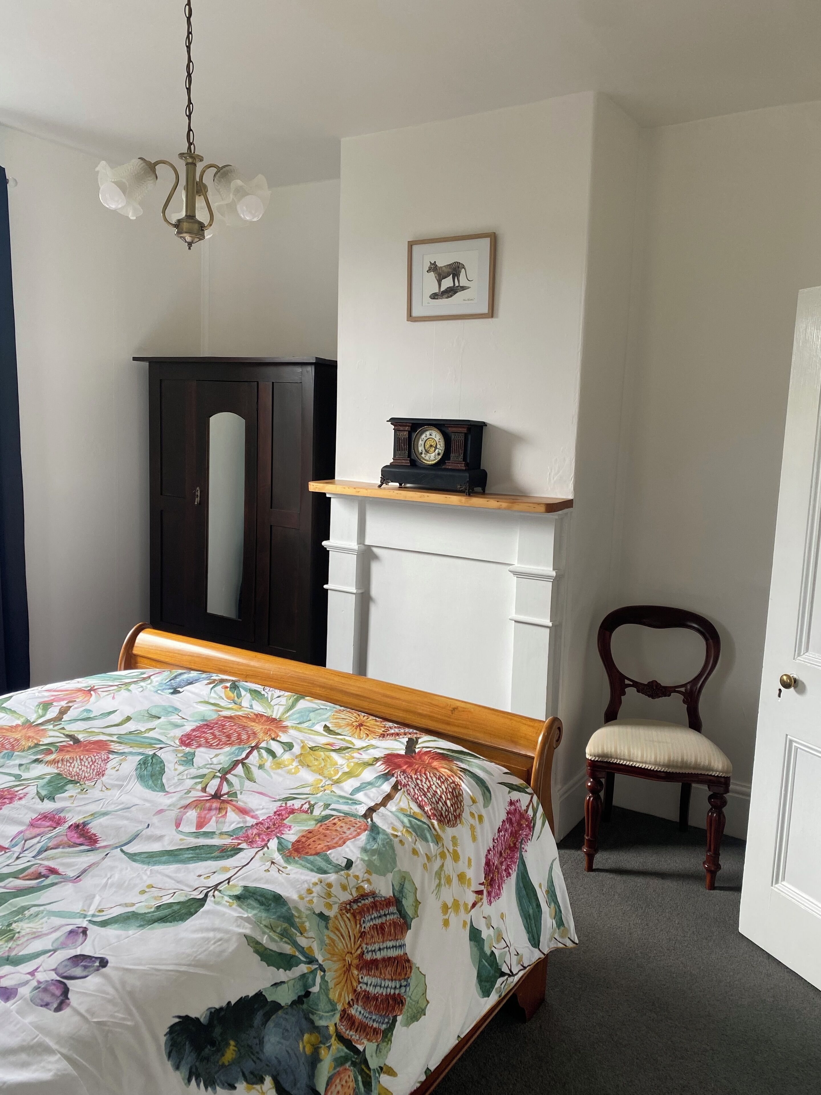 Une chambre à coucher avec un lit, une chaise en bois, une commode, une horloge et un tableau encadré accroché au mur.