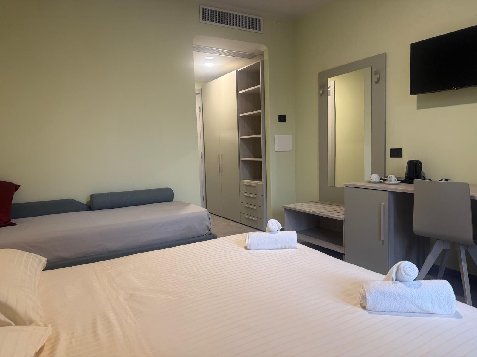 Ein Hotelzimmer mit zwei Betten, einem Schreibtisch mit Stuhl, einem Fernseher und einem Kleiderschrank.