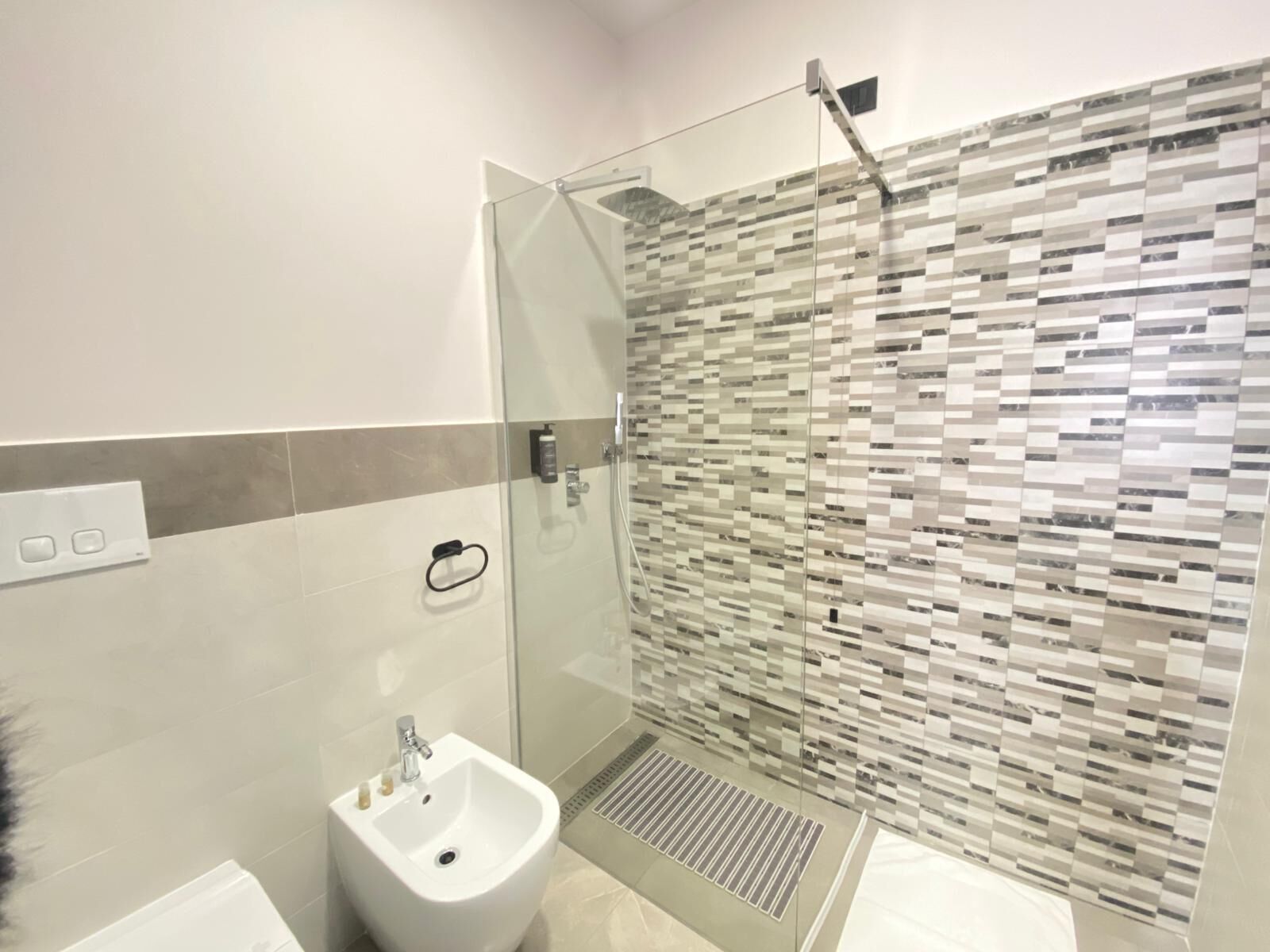 Ein modernes Badezimmer mit einer Duschkabine, einem weißen Standwaschbecken und einer gefliesten Duschwand.