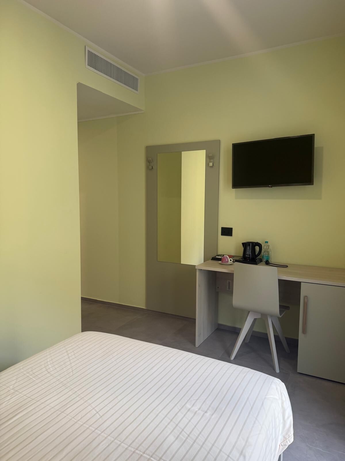 A hotel room with a bed, a desk, a chair, a television, and a mirror.