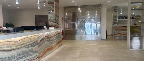 A reception desk with a marble top, a large glass door with a metal frame, and a modern interior with recessed lighting.