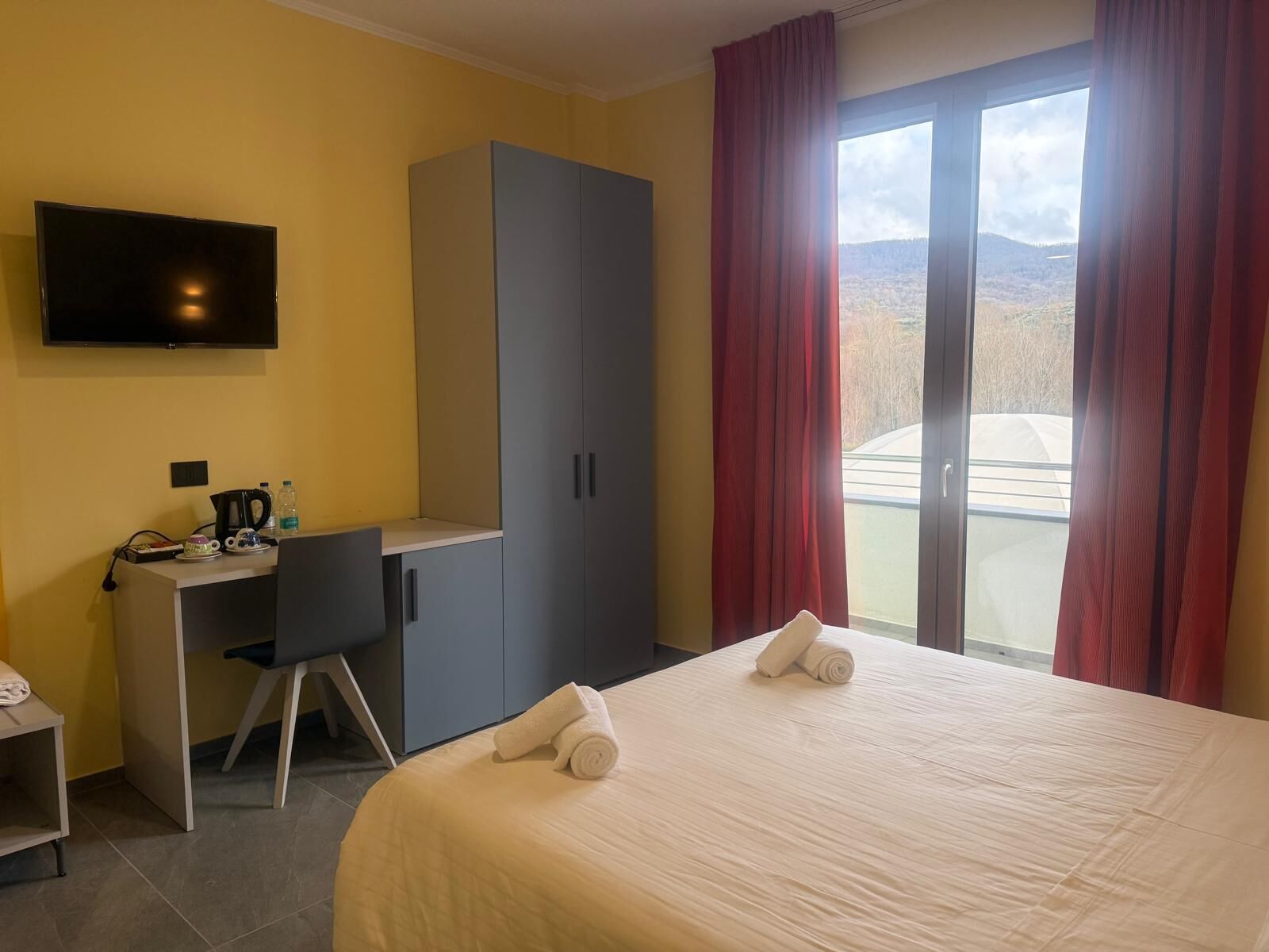 Una habitación de hotel con cama, escritorio con silla, televisor y armario.