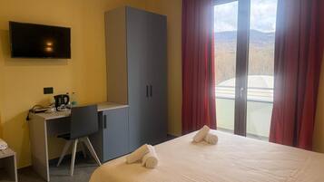 Una habitación de hotel con cama, escritorio con silla, televisor y armario.