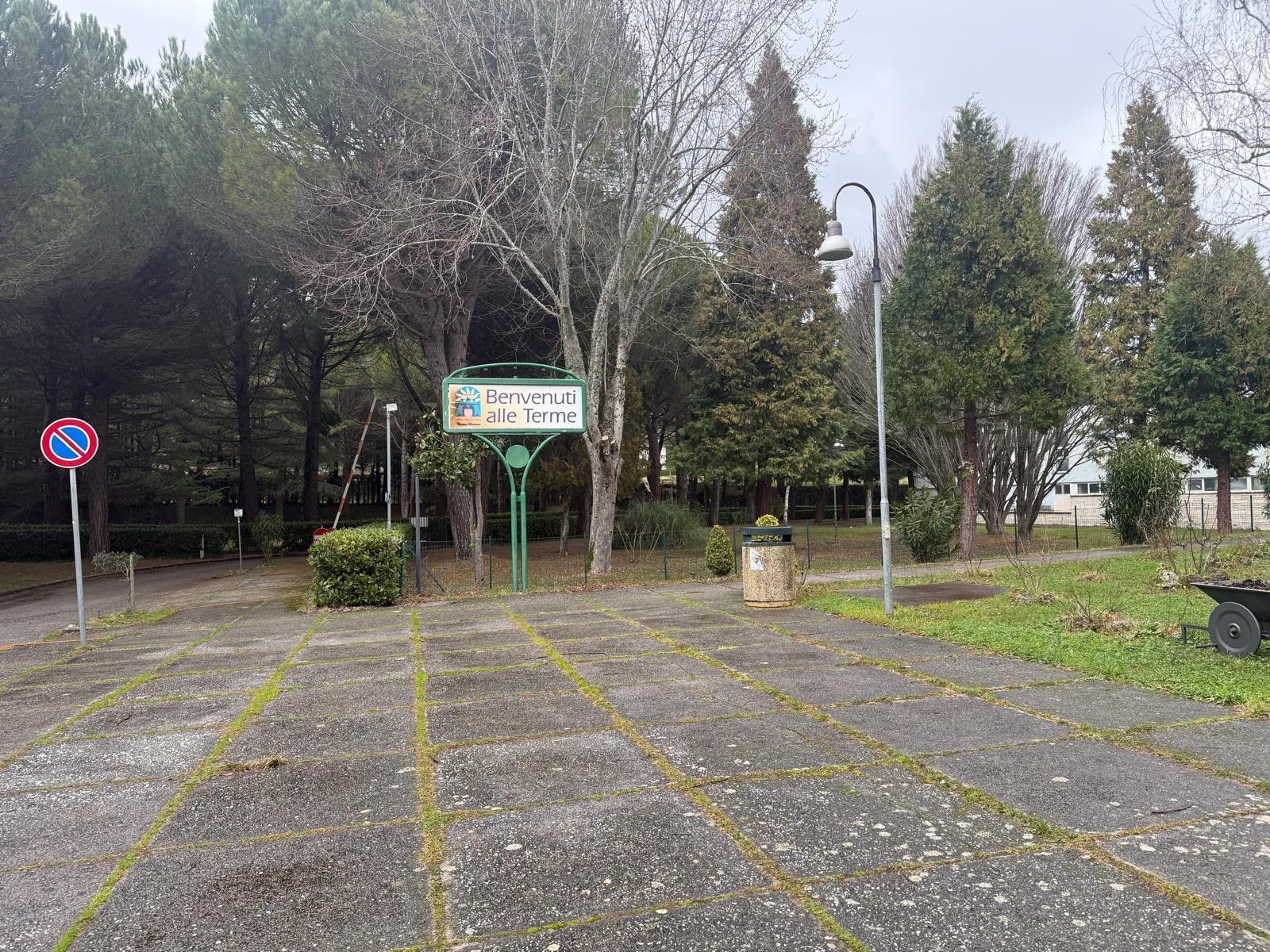 A paved area with a no parking sign, a welcome sign, and a trash bin.