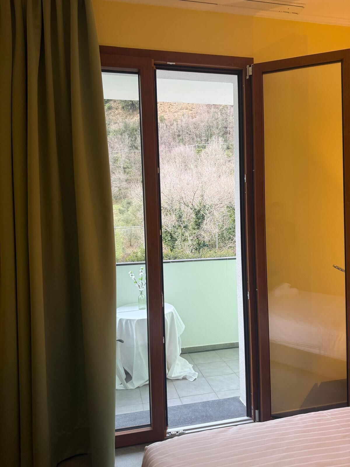 Quarto com cama, uma mesa com um vaso e vista para uma varanda com mesa e cadeiras.