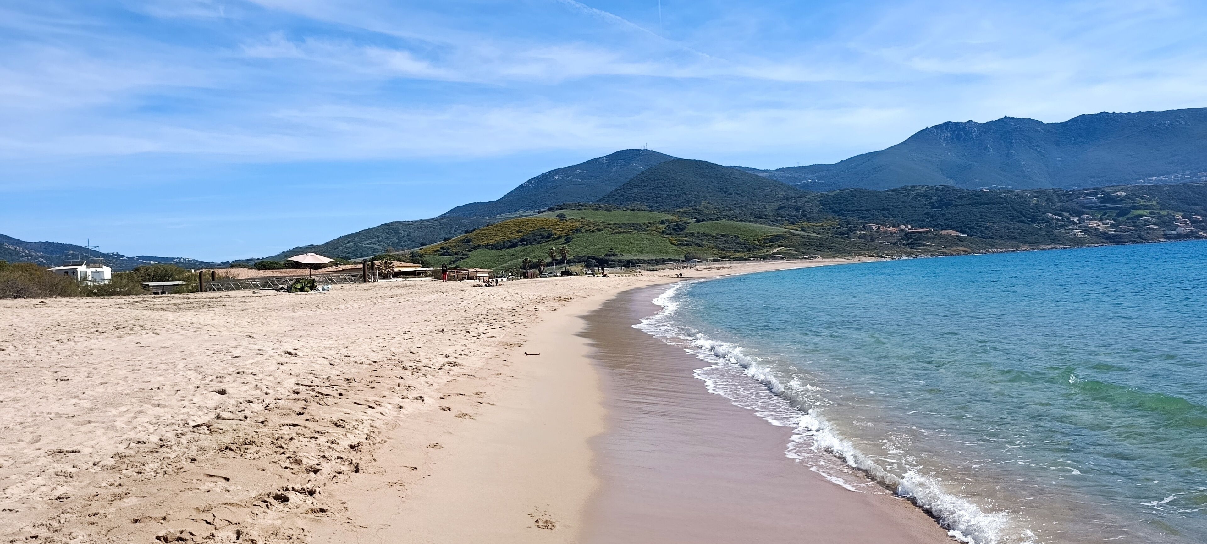 Une plage à l’eau claire, avec un rivage sablonneux et des montagnes en arrière-plan.