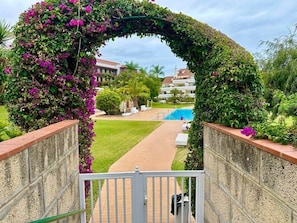 Un camino al aire libre que conduce a una zona de piscina, rodeada de exuberante vegetación y un arco decorativo.