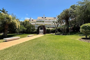 Un jardín bien cuidado con un sendero que conduce a un edificio de fachada blanca y techo de tejas.