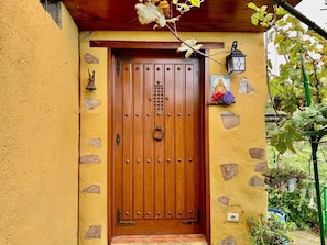 A wooden door with a knocker, a bell, and a small shelf with a picture and flowers. - Finca Las Madrecitas (La Orotava)
