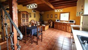 Uma cozinha rústica com armários de madeira, uma mesa de jantar com cadeiras, uma escada e uma janela que ilumina o espaço com luz natural.