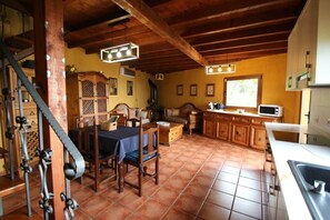 A rustic kitchen with wooden cabinets, a dining table with chairs, a staircase, and a window providing natural light. - Finca Las Madrecitas (La Orotava)