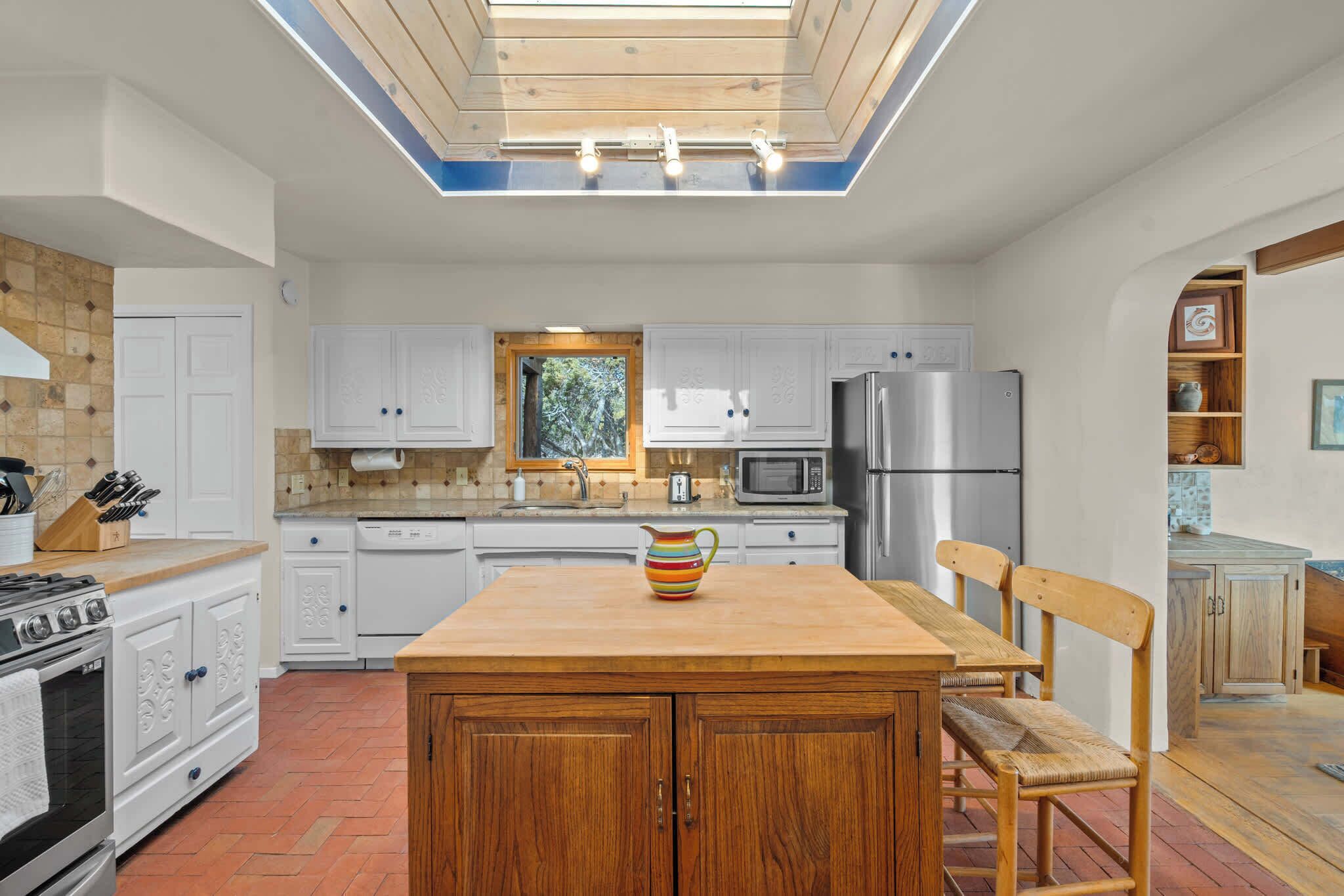 A modern kitchen with white cabinets, a wooden island, and a skylight.