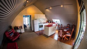 A compact kitchen with a central island, a dining area with a table and chairs, and a red armchair.