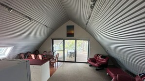 A compact, sloped-roofed room with a dining area, a sofa, and a refrigerator.