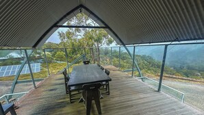 A covered outdoor area with a table and chairs, overlooking a forested landscape and solar panels.