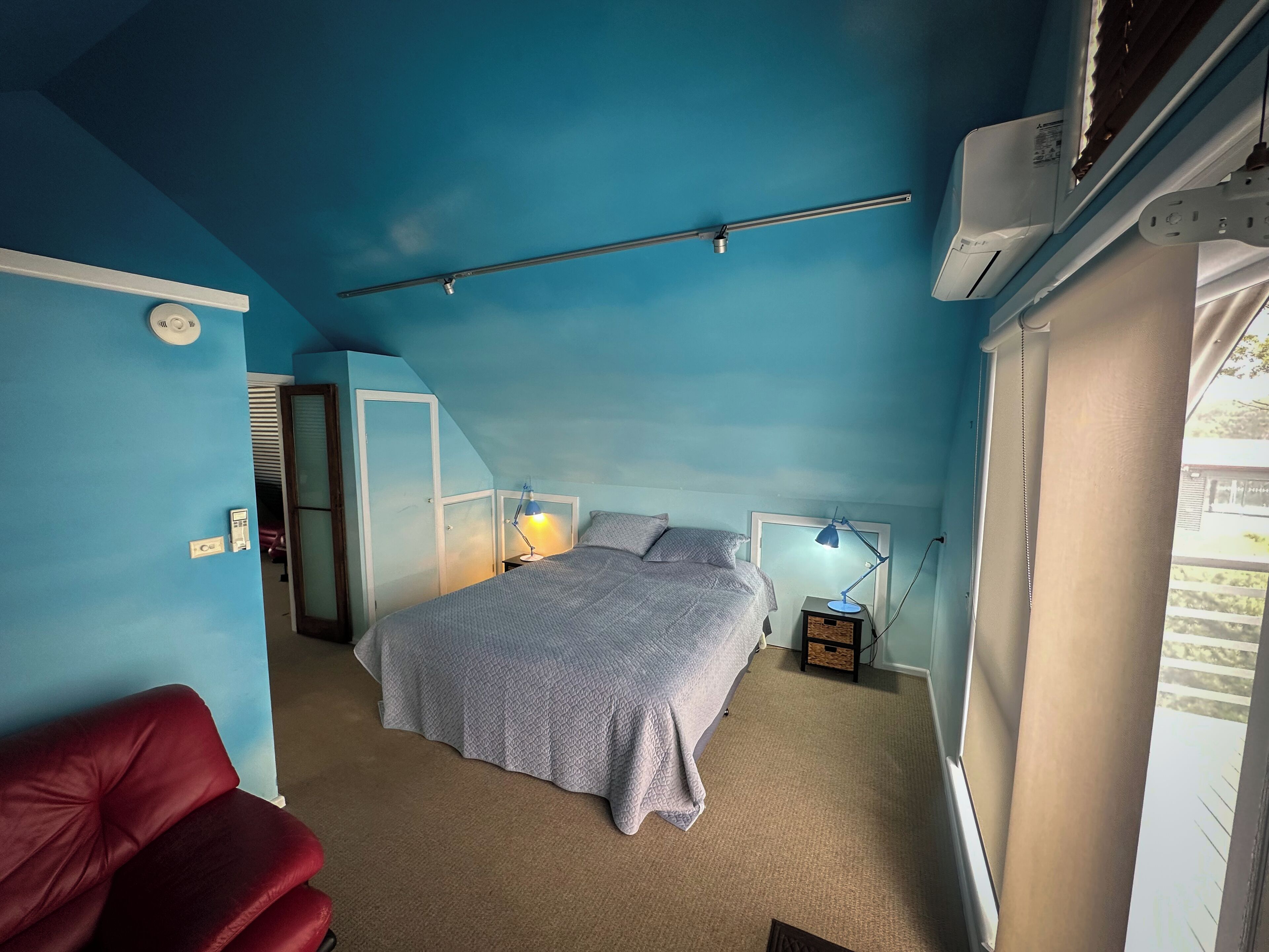 Un dormitorio con cama, lámparas de noche, una silla roja y una ventana.