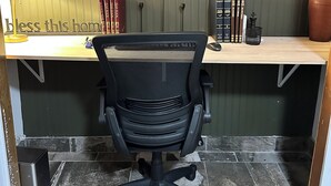 A home office with a wooden desk, black office chair, and books.