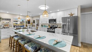 A modern kitchen with white cabinetry, stainless steel appliances, and a central island with stools. - NEW! Waterfront Gulf Retreat w/ Heated Pool, Spa, & Mini Golf. (Hernando Beach)