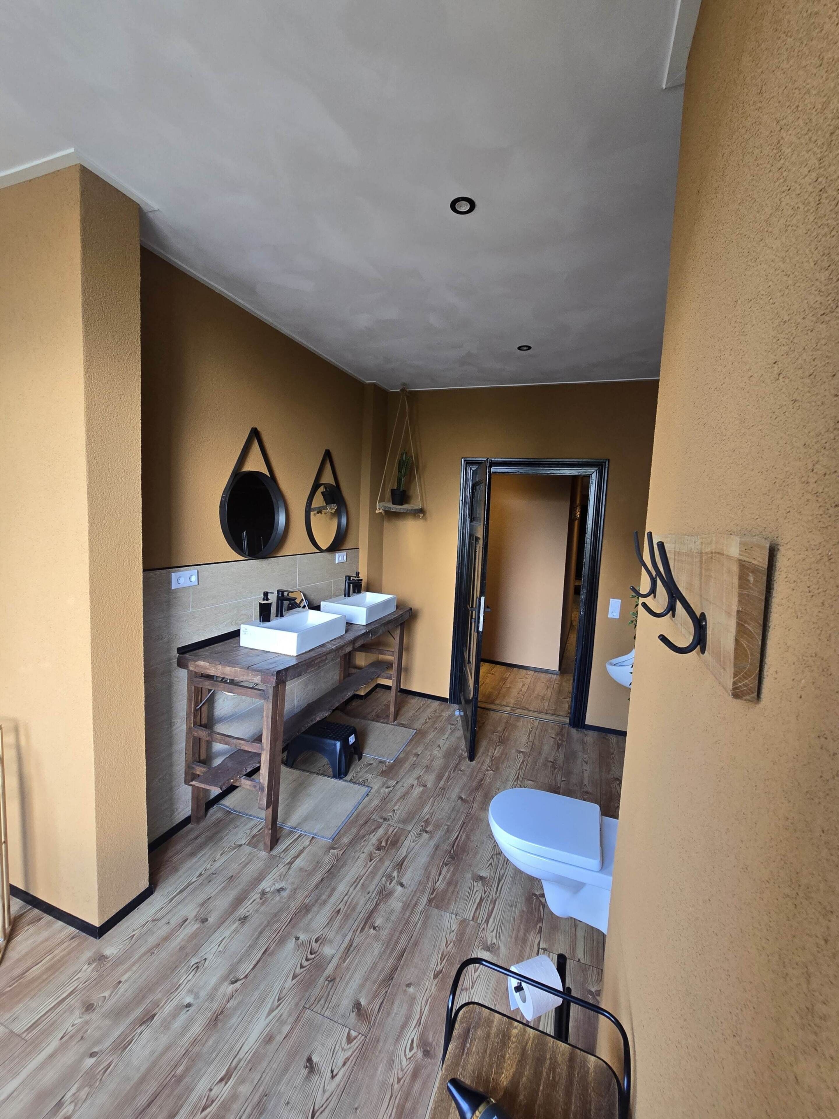 Une salle de bain avec un plancher en bois, un lavabo avec un miroir et des toilettes.