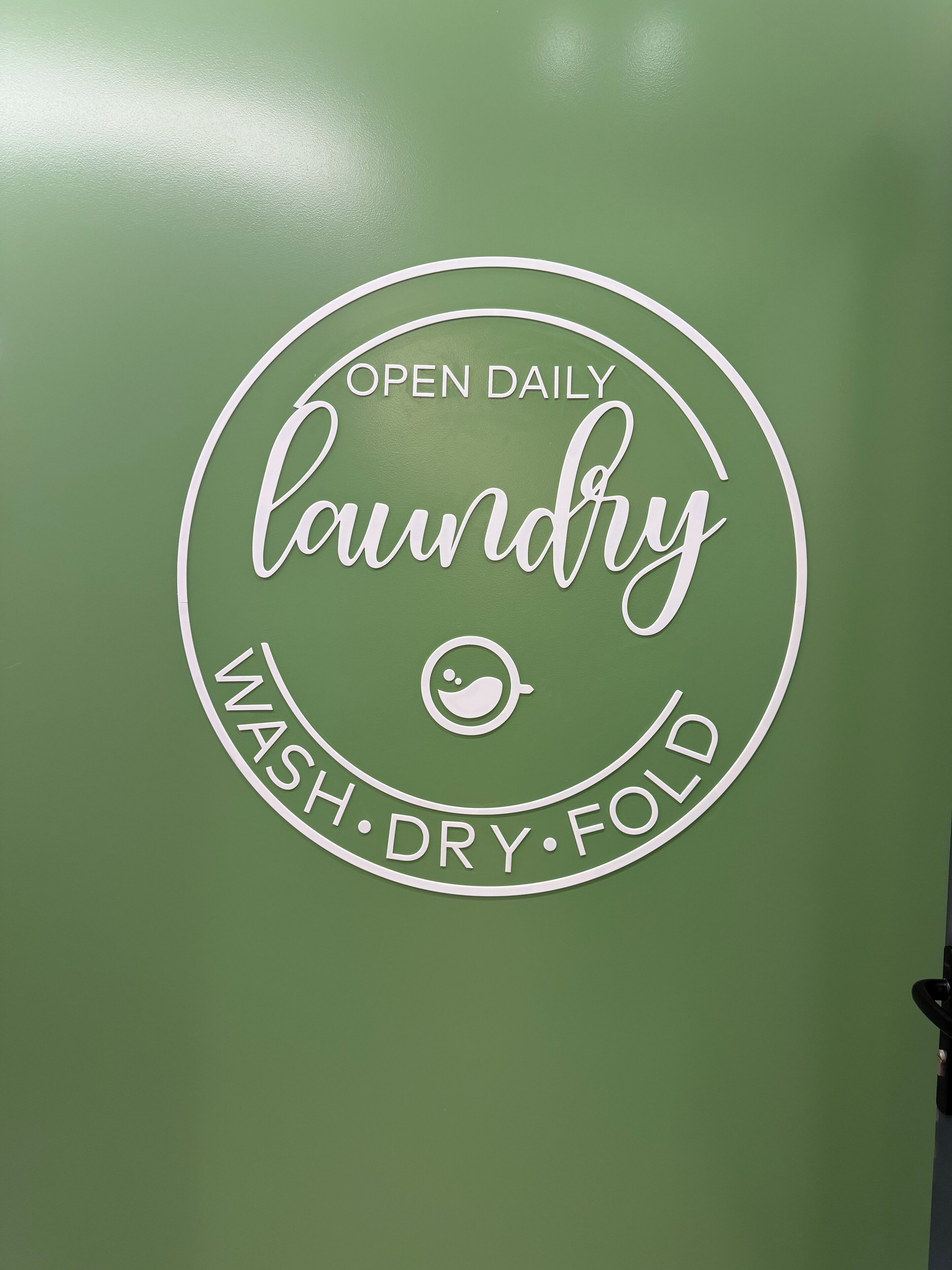 Un muro verde con un cartello circolare che recita 'OPEN DAILY laundry WASH DRY FOLD'.