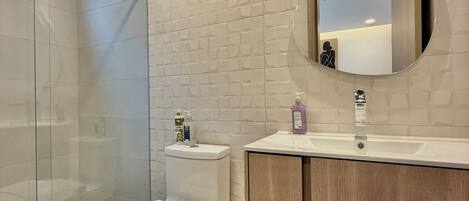 Un bagno moderno con cabina doccia in vetro, un water, un lavabo con specchio e un lavandino.