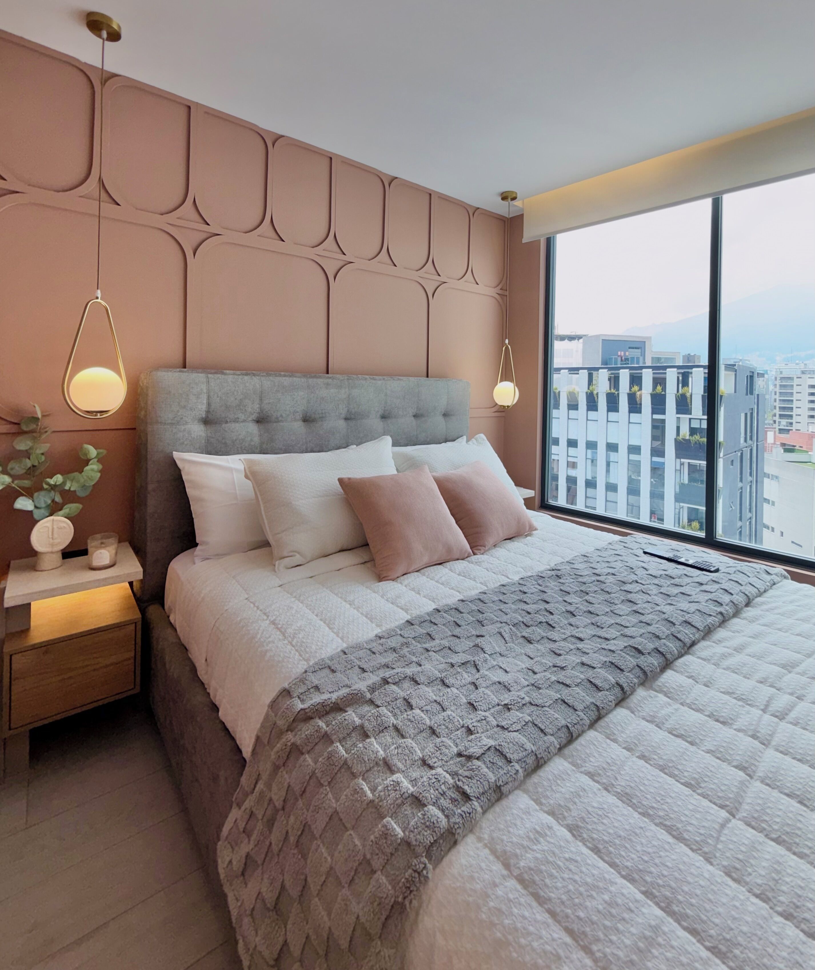 A modern bedroom with a large bed, a nightstand, and a window with a city view.