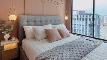 A modern bedroom with a large bed, a nightstand, and a window with a city view.