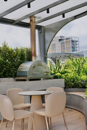 Une terrasse extérieure équipée d’un barbecue en acier inoxydable, d’une table ronde et de quatre chaises.