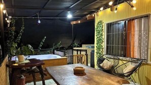 An outdoor patio with a wooden table and benches, surrounded by potted plants and string lights. - Vista Lapas Vacation Home (Quepos)