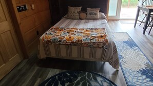 Een slaapkamer in een houten blokhut, met een bed, een nachtkastje, een wandlamp en een deur naar een balkon.