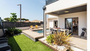 Een modern buiten terras met een zwembad, zitgedeelte en een overdekte eethoek.