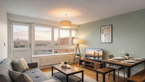A modern living room with a sofa, coffee table, TV, and dining area. - Shepherd’s Bush • 2 Bed with Terrace • Westfield • (London)
