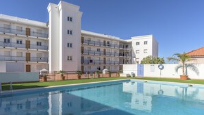 A swimming pool with a clear blue water surface, surrounded by a white building with multiple balconies and a central tower. - FLH Vila Real Santo António Colourful Apartment (Vila Real de Santo António)