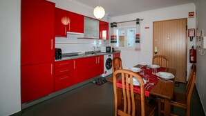 A compact kitchen with red cabinets, a dining table set for four, and a wooden door. - FLH Vila Real Santo António Colourful Apartment (Vila Real de Santo António)