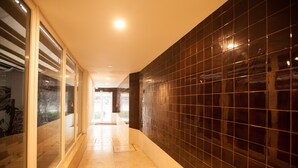 Un couloir avec un mur recouvert de carreaux et une porte en verre sur le côté gauche.