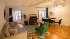 Un salon comprenant un canapé, un fauteuil vert, une table à manger avec des chaises, un téléviseur et une plante en pot.