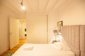 A hotel room with a bed, a bedside table, a lamp, and a door leading to another room. - FLH Intendente Chic Apartment with Rooftop Pool (Lisboa ciudad)