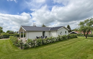 A single-story house with a covered patio, surrounded by a well-maintained lawn and hedges.