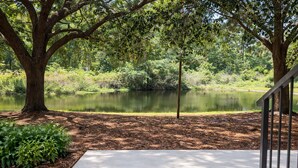 A serene outdoor area with a concrete path, a metal railing, and a pond surrounded by trees. - 2 Bedroom 4 Min to Universal + Free Parking + Fast WiFi (Orlando)